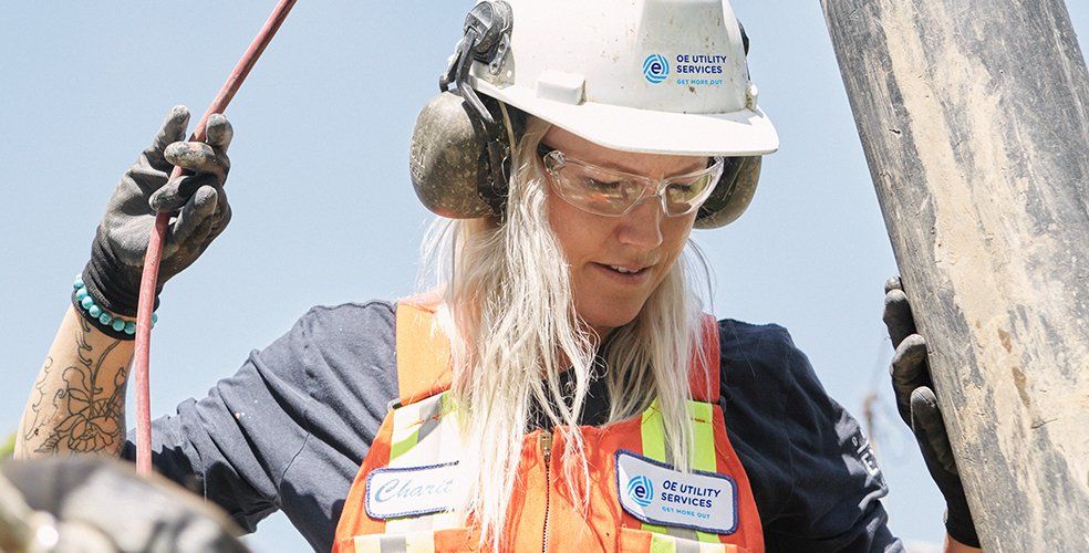 Woman in safety gear working outdoors, holding cable, focused.