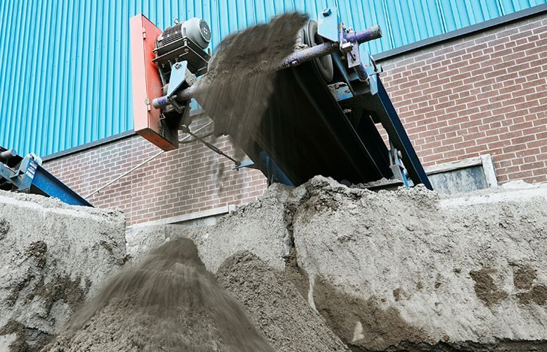 Industrial conveyor belt depositing sand onto a pile.