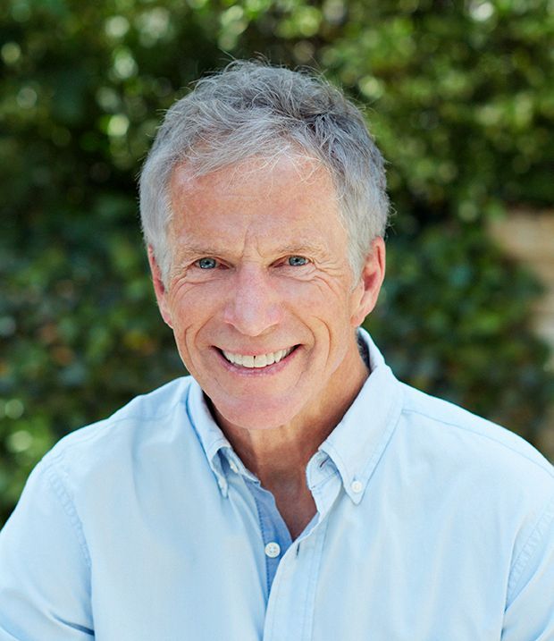 Smiling man in a light blue shirt outdoors, blurred green background.