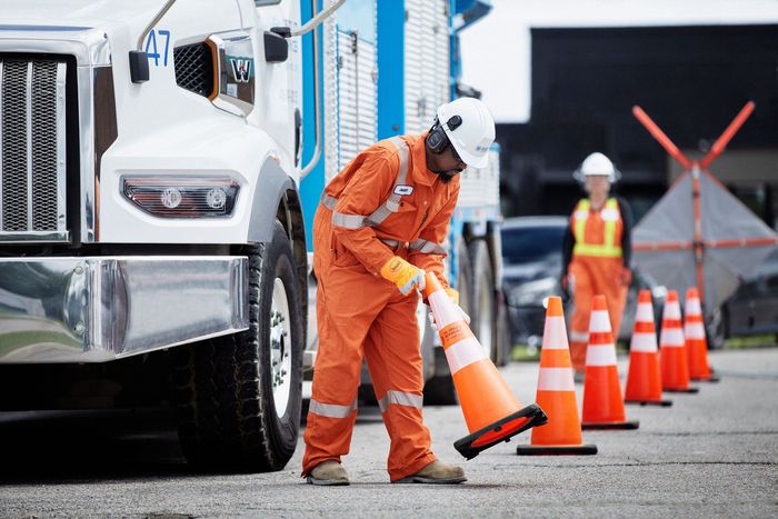 Worker in orange uniform placing traffic cones near a large truck.