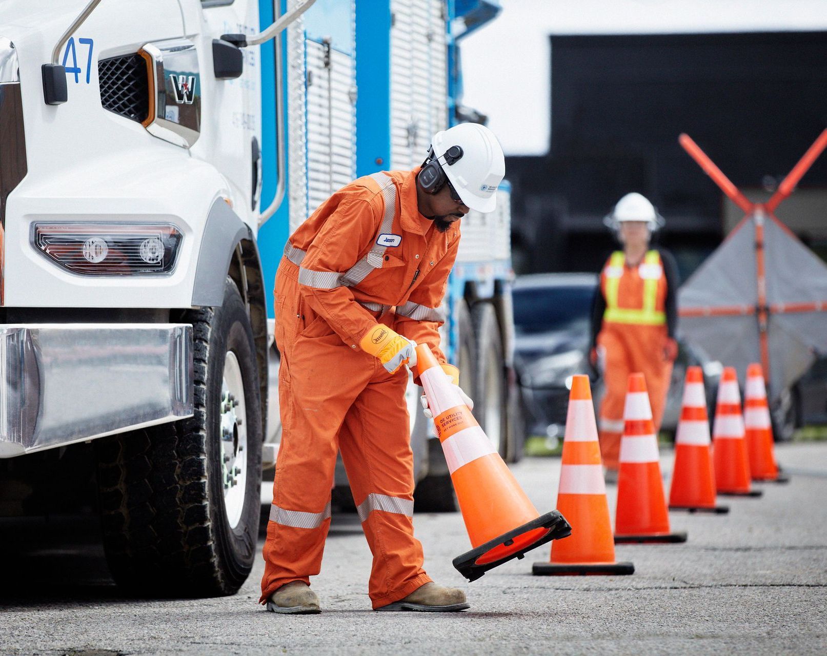 Worker in orange jumpsuit placing traffic cones near truck.