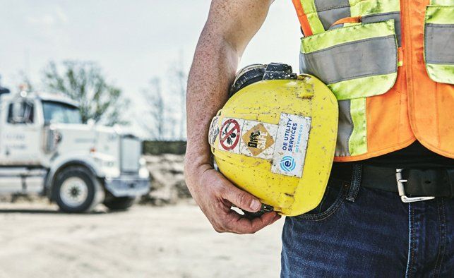 Person in safety vest holding a yellow container with hazard labels in front of a truck.