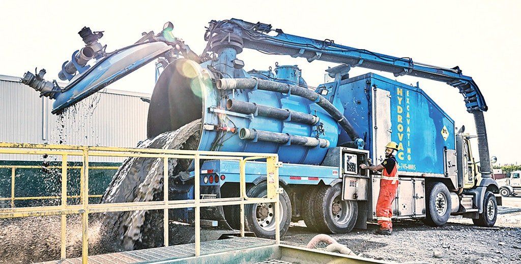 Blue industrial truck with articulated arm, operator in orange suit, handling debris, outdoor setting.