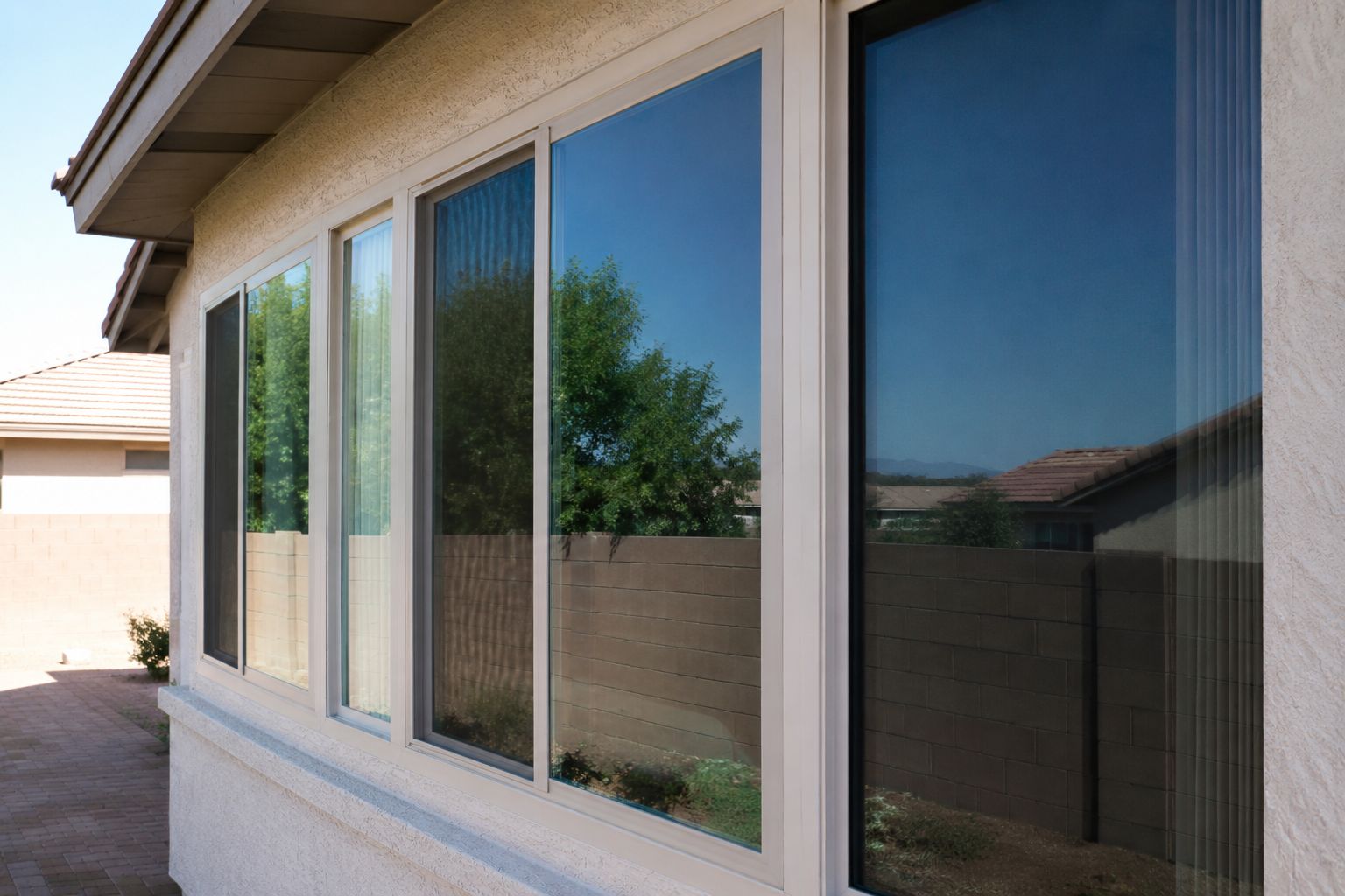 Exterior view of a house wall with large reflective windows and a beige stucco frame