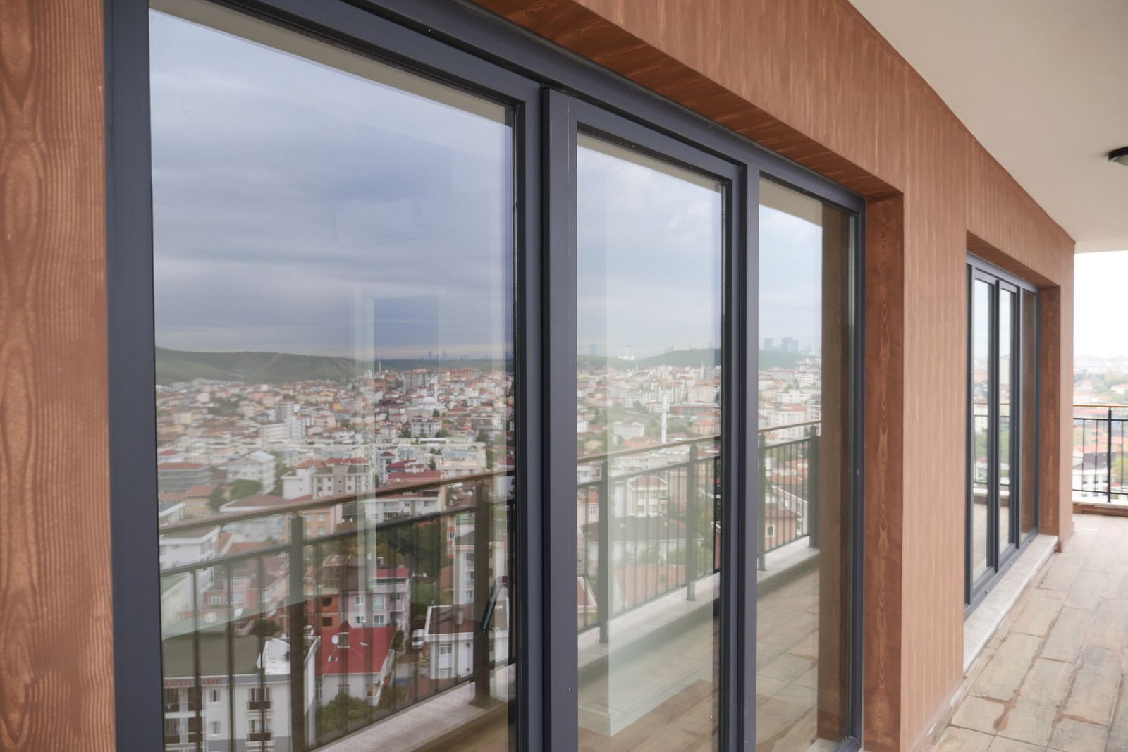 Balcony with large glass sliding doors overlooking a city. Gray frames, wood-look siding.