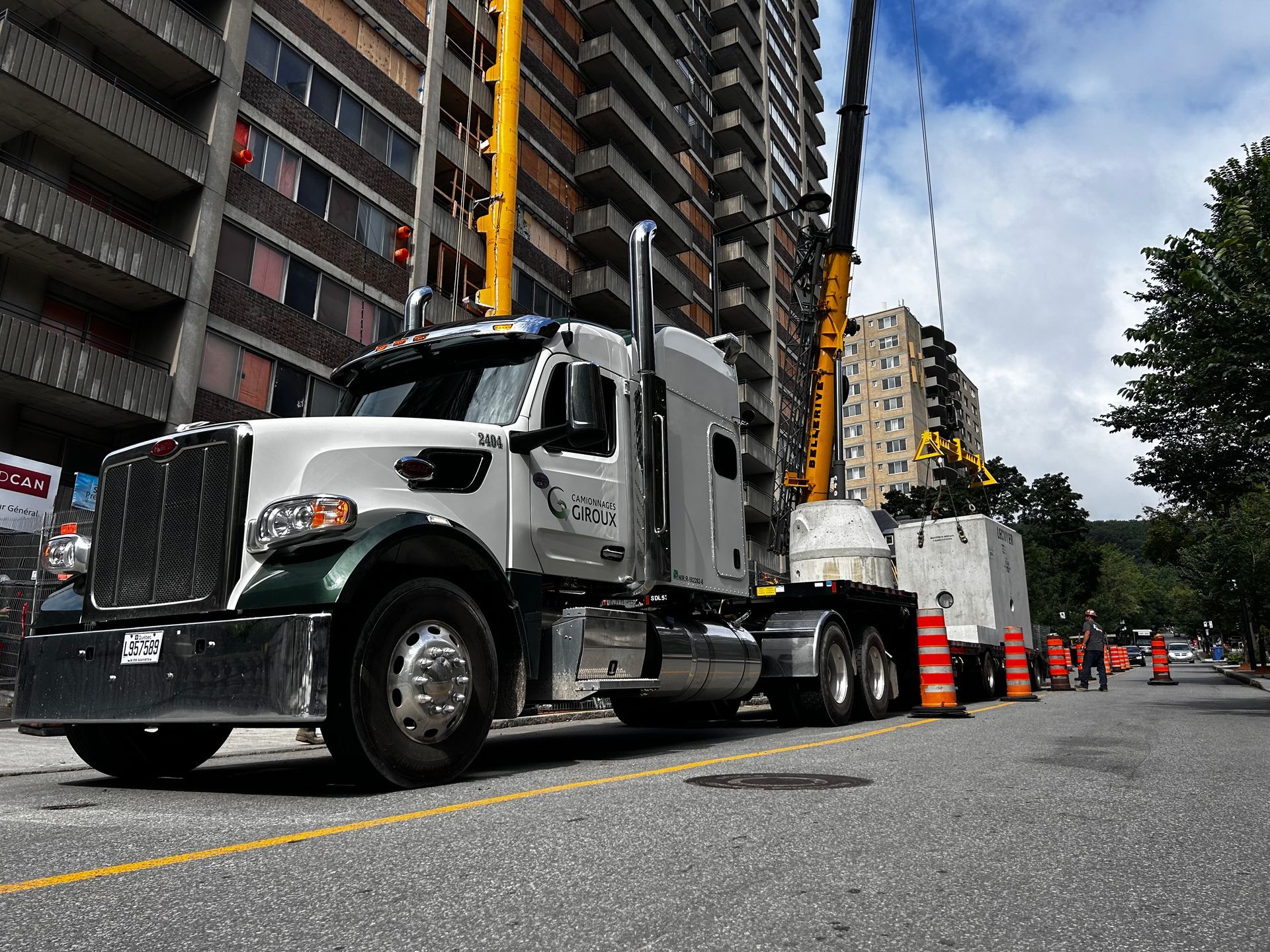 A semi truck is parked on the side of the road in front of a tall building.