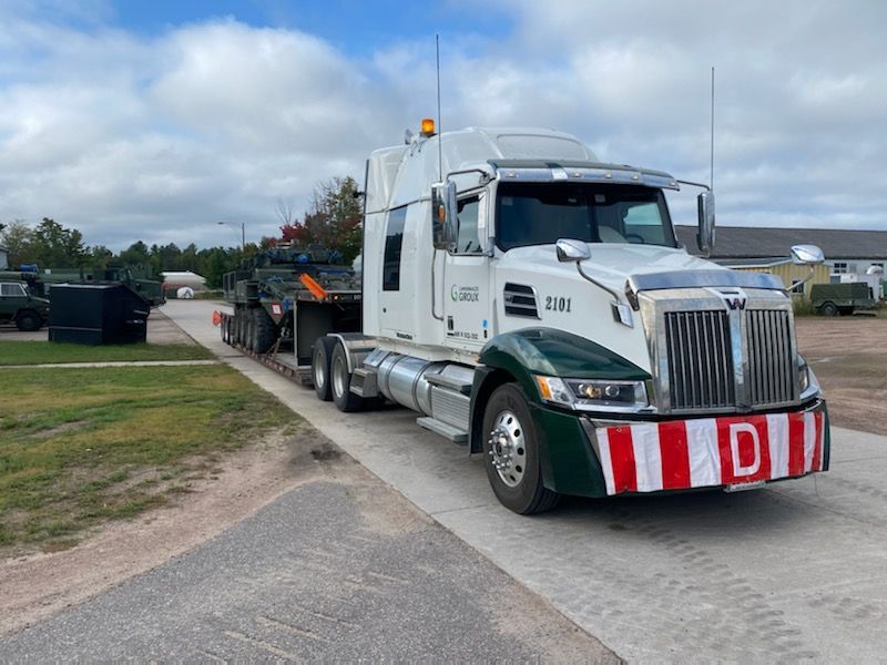 A semi truck is carrying a military vehicle on a trailer.
