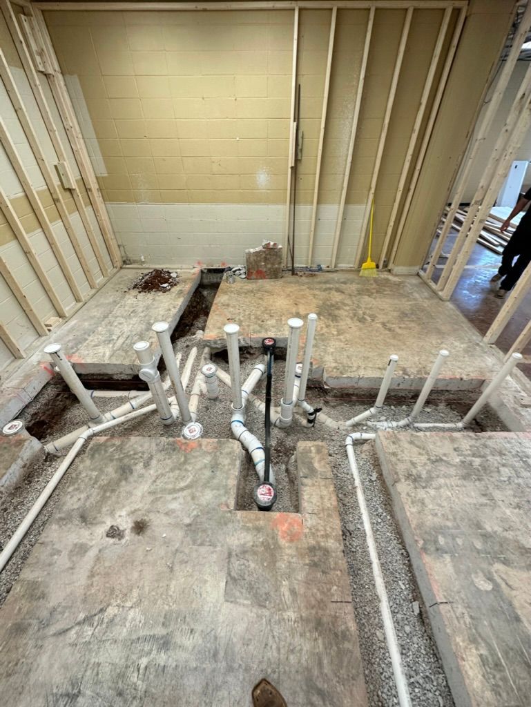Construction site with exposed floor joists and several white PVC pipes protruding from concrete.