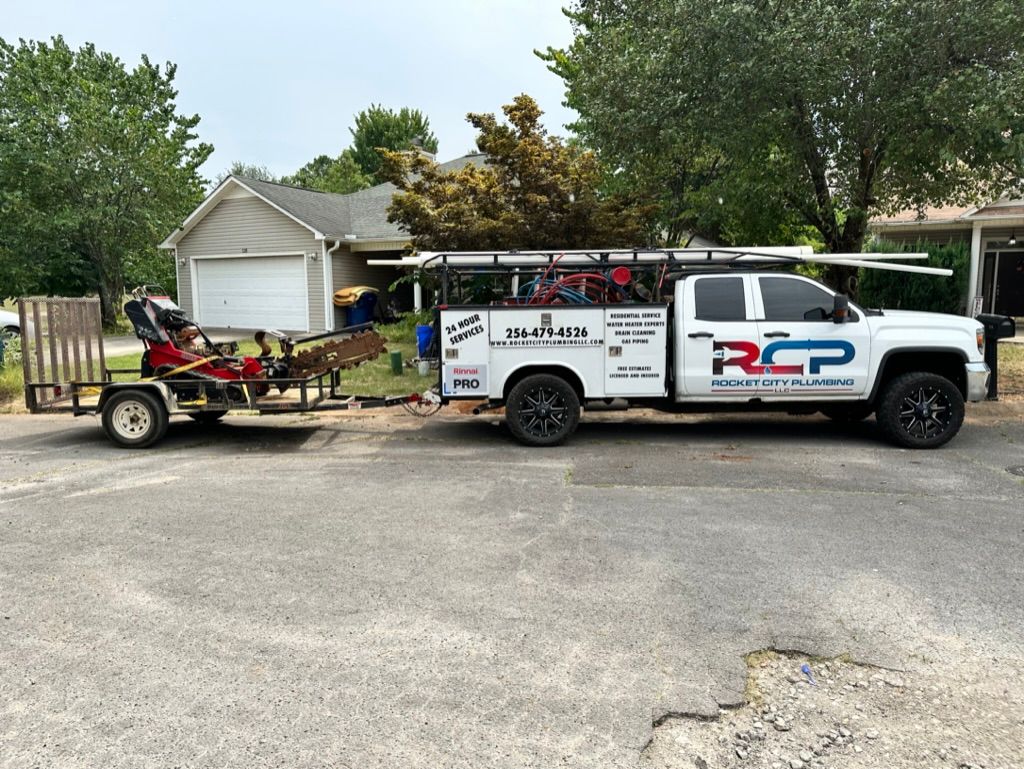 White RCP service truck towing a trailer with equipment parked in a driveway by a garage and trees