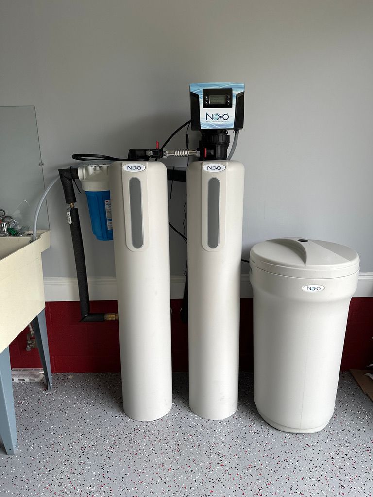 Three white water filter tanks beside a white cylindrical container in a utility room with a speckled floor