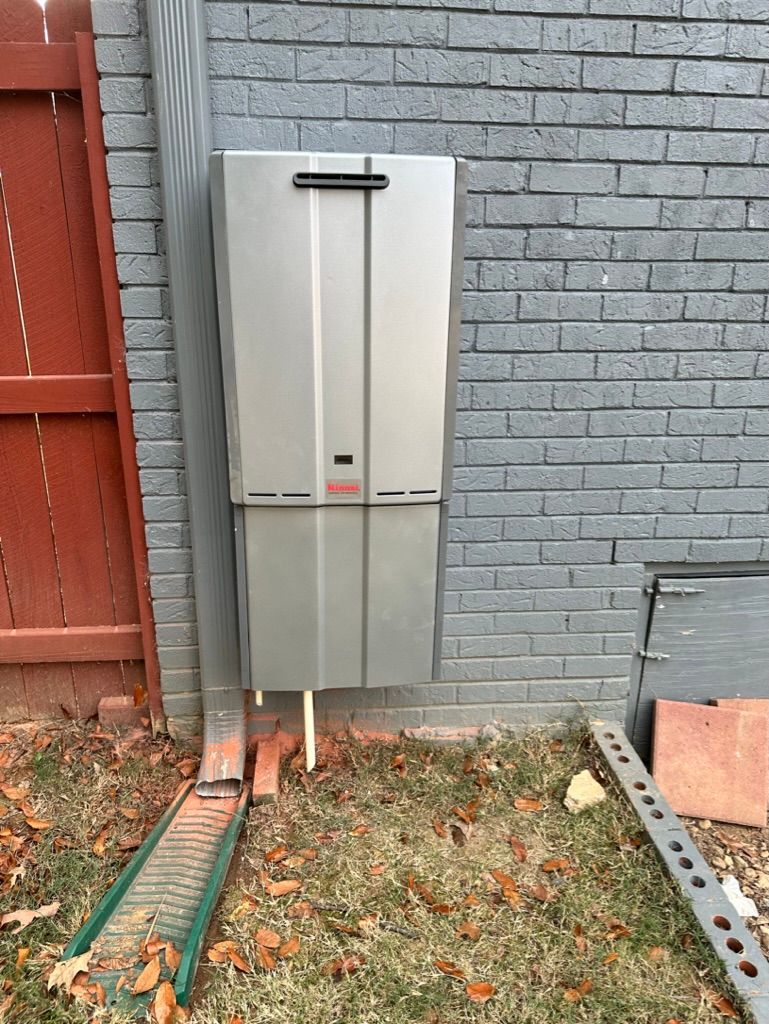 Outdoor utility box mounted on a gray brick wall beside a fence and fallen leaves