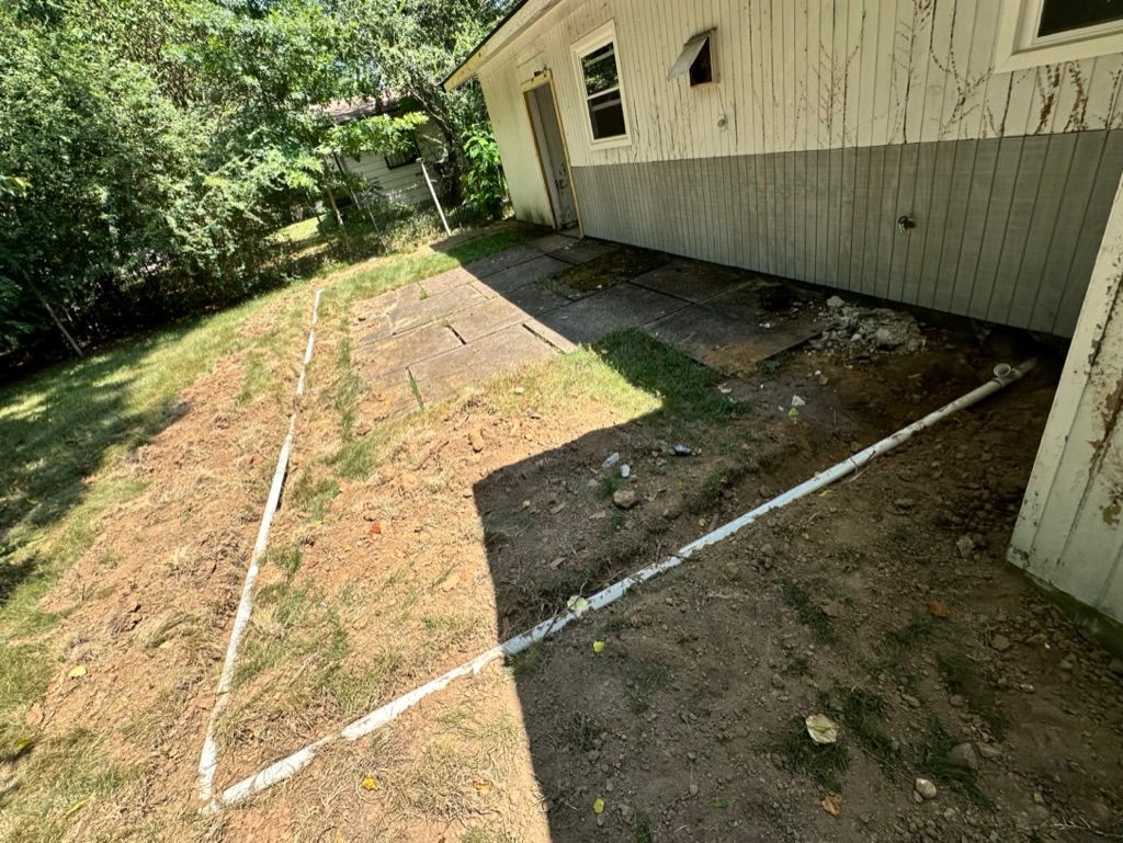 Grassy backyard beside a house, with white boundary lines marking a sloped area.