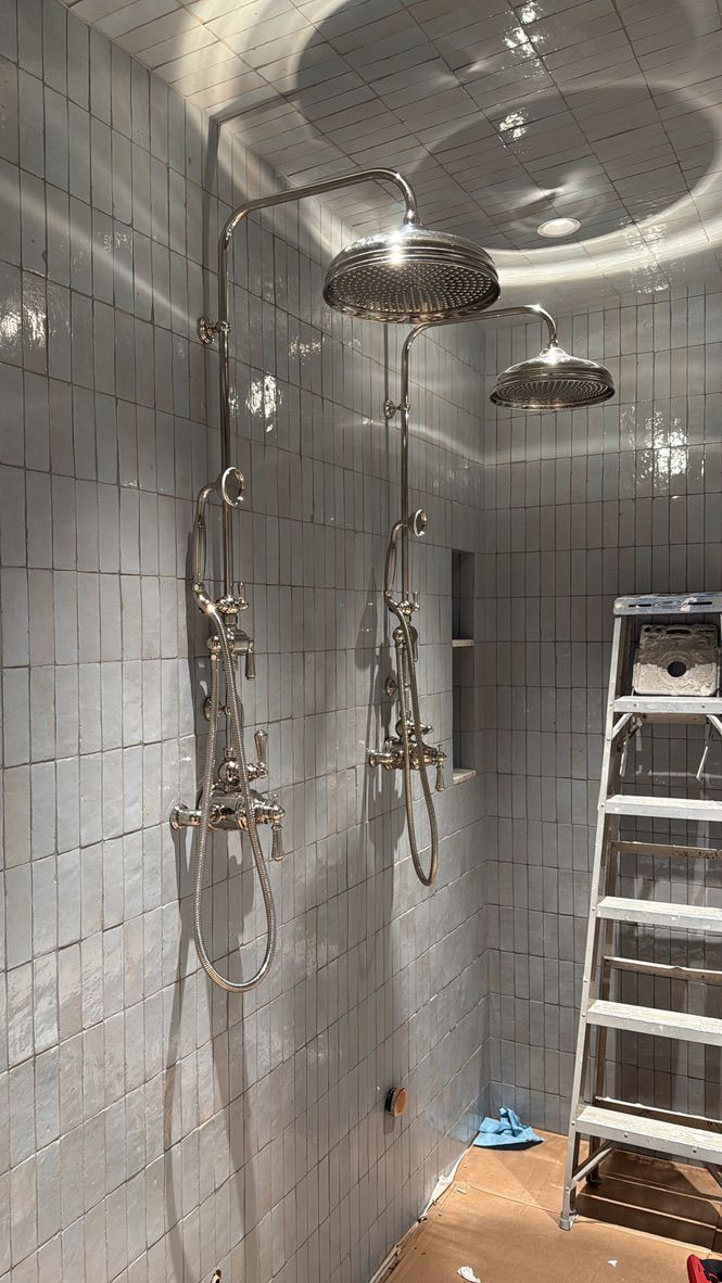 Small unfinished room with tiled walls, hanging fixtures, a ladder, and exposed wiring or pipes.