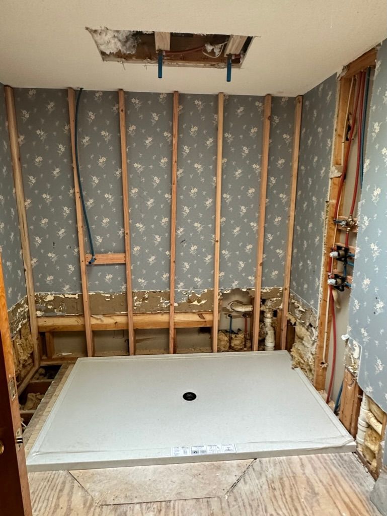 Bathroom under renovation with exposed studs, insulation, and a white shower base installed.