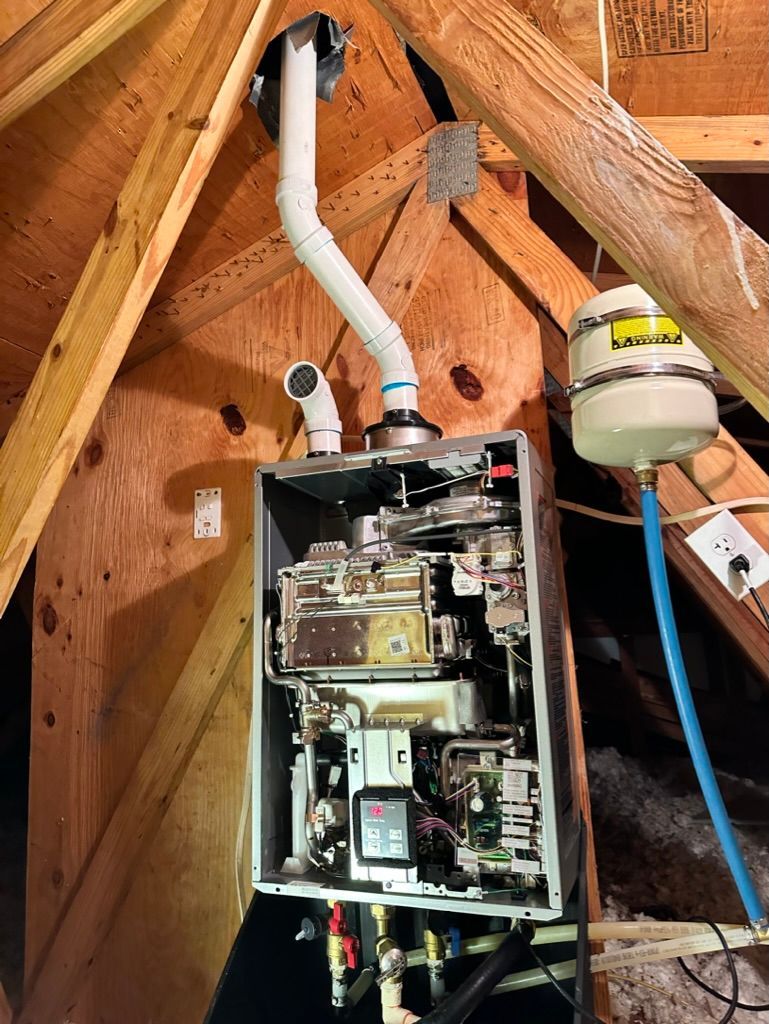 Open electrical panel with exposed wiring in an attic near a white PVC vent pipe and small tank.
