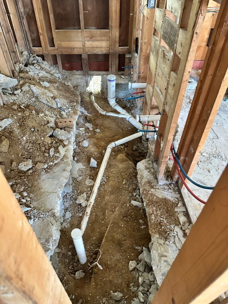 Exposed plumbing pipes in a dirt crawl space during home renovation
