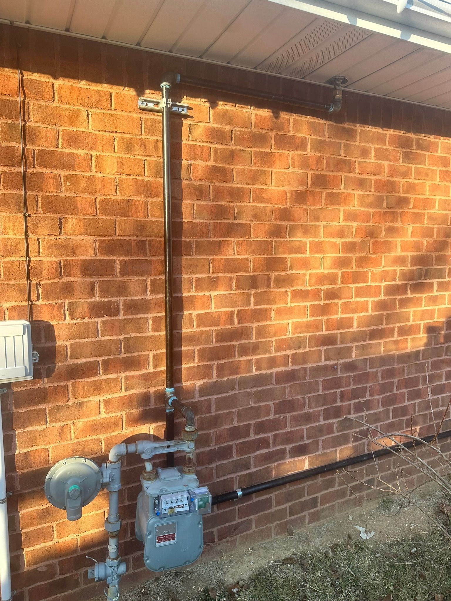 Gas meter and vertical pipe mounted on a brick wall beside a house eave.