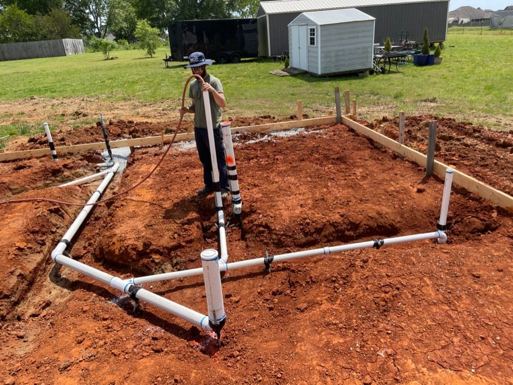 PVC pipe layout on red dirt in a backyard, with a small shed and grass in the background