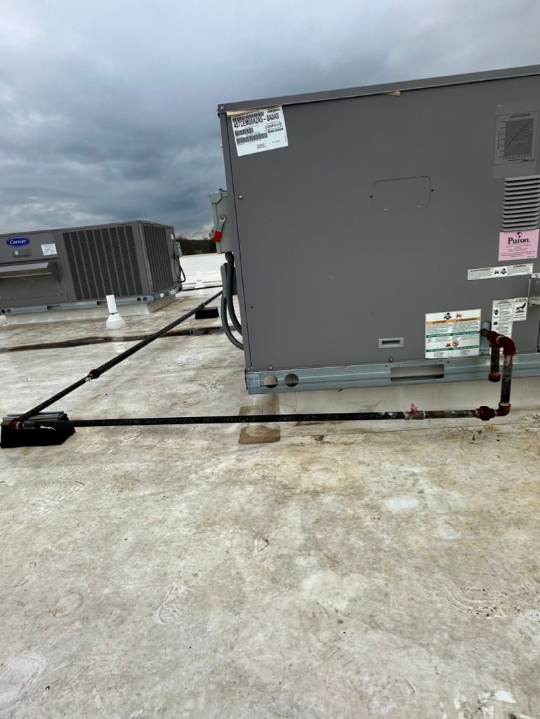 Rooftop HVAC unit with attached pipes and hoses under a cloudy sky.