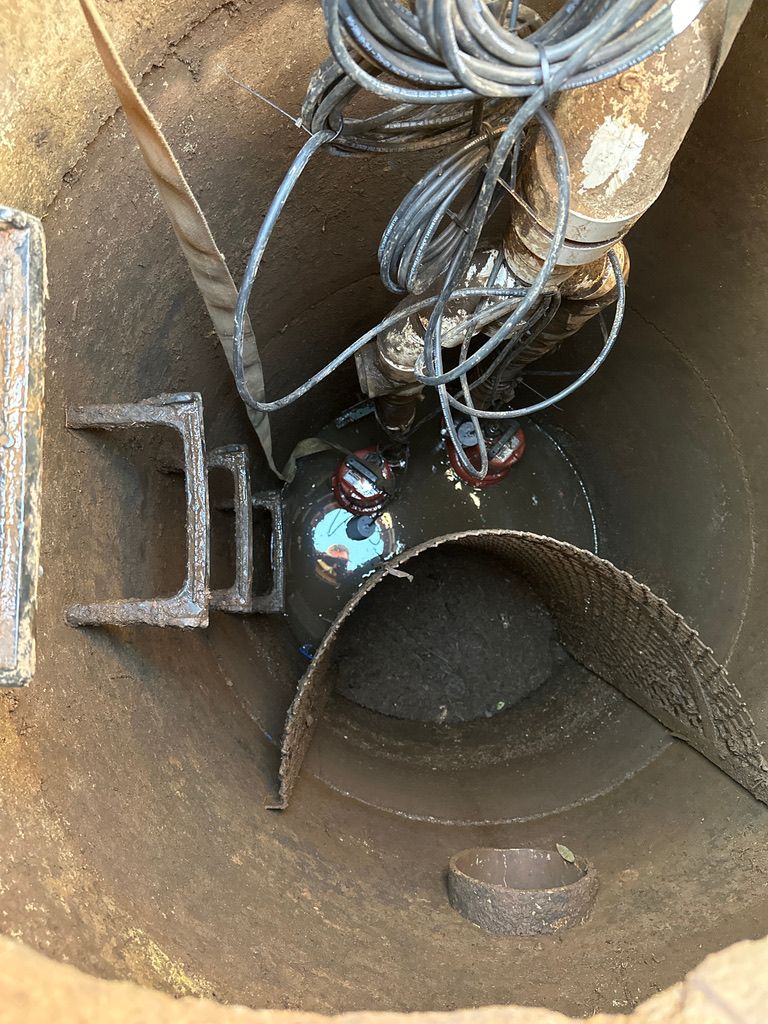 Inside a narrow metal shaft, a curved pipe and bundled cables are visible above a rusty interior.