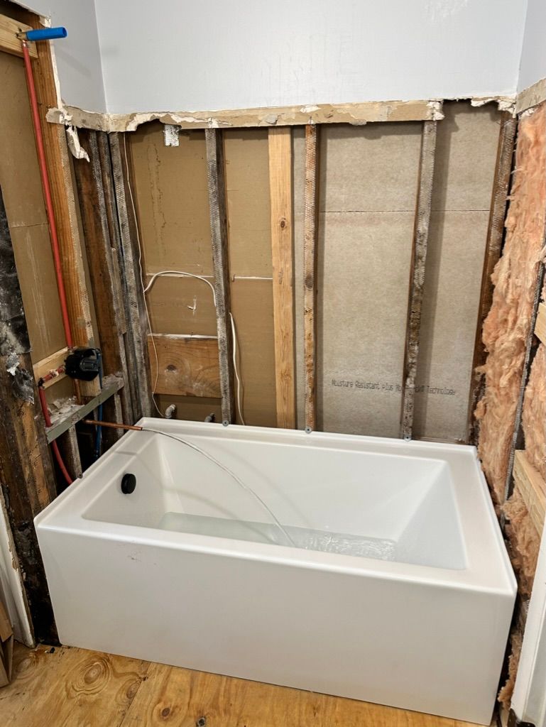 White bathtub installed against exposed wall studs during bathroom renovation
