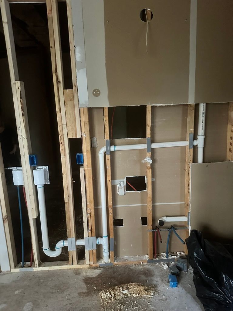 Exposed bathroom wall framing with plumbing pipes, valves, and unfinished drywall during renovation