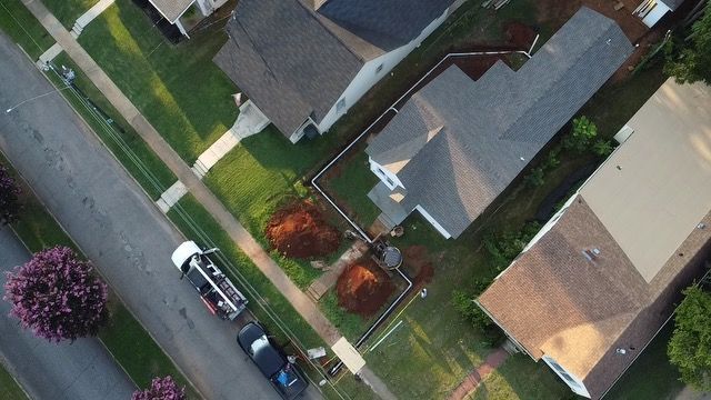 Aerial view of a suburban street with parked cars, sidewalks, and houses with yards and trees.