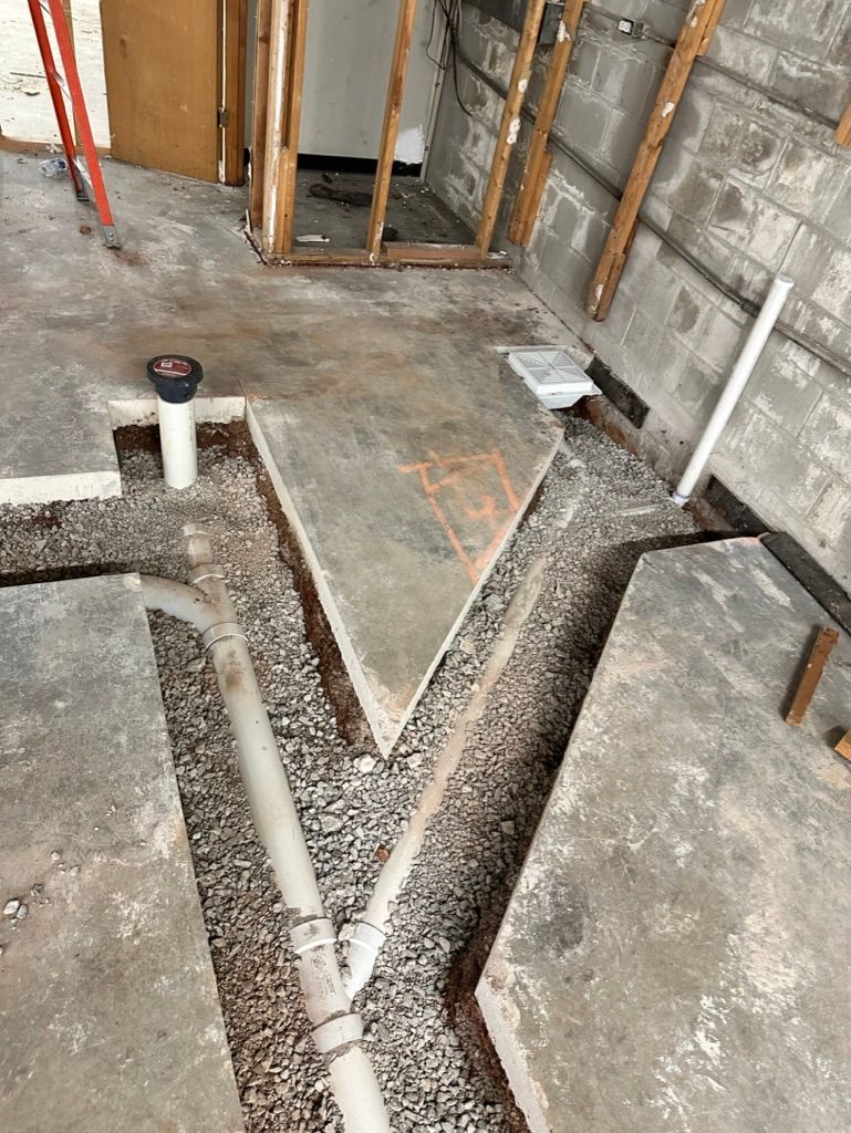 Construction site floor with exposed trenches, white PVC pipes, and unfinished concrete walls