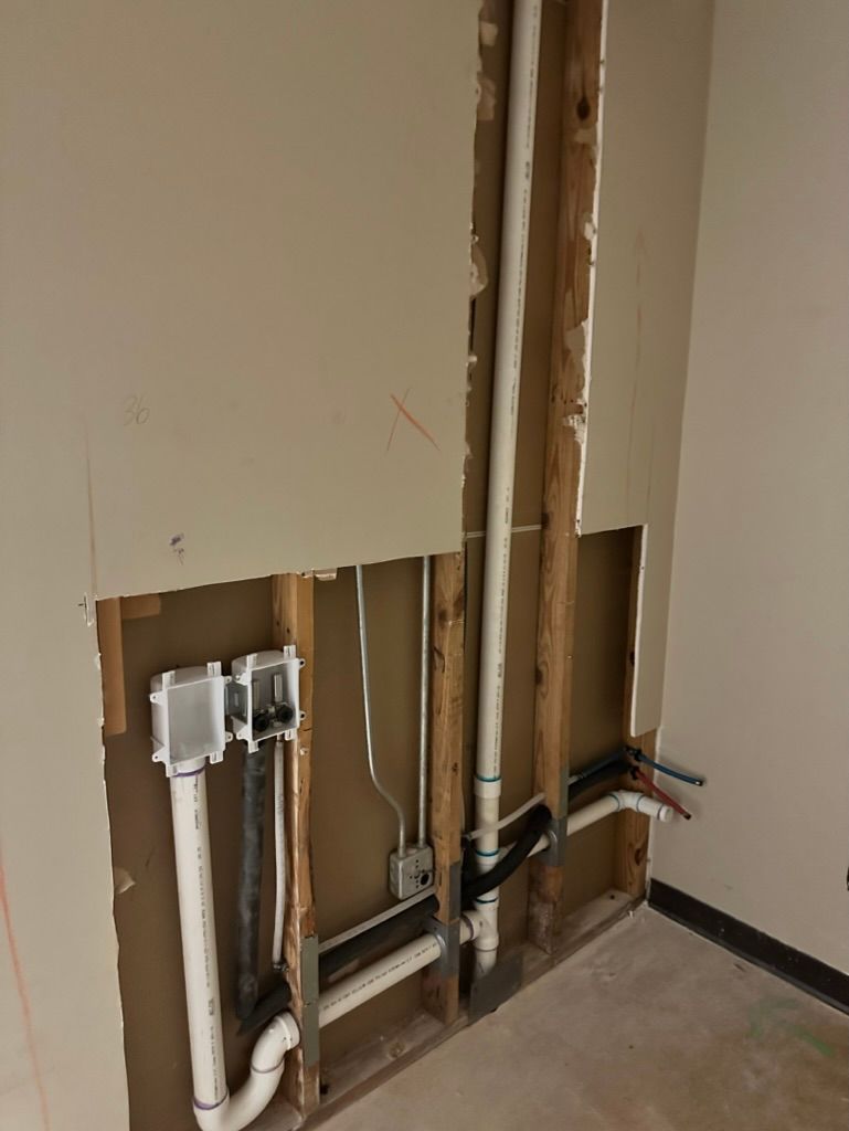 Bathroom wall cut open, exposing plumbing pipes and electrical box inside the studs.