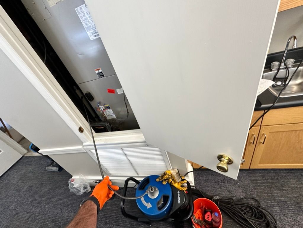 Open electrical panel beside a white wall, with tools and cables on carpeted floor.