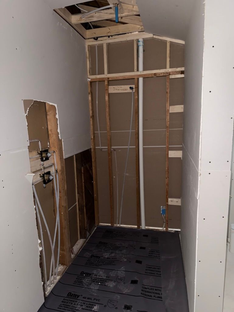 Narrow hallway under construction with exposed framing, unfinished drywall, and a black floor mat.