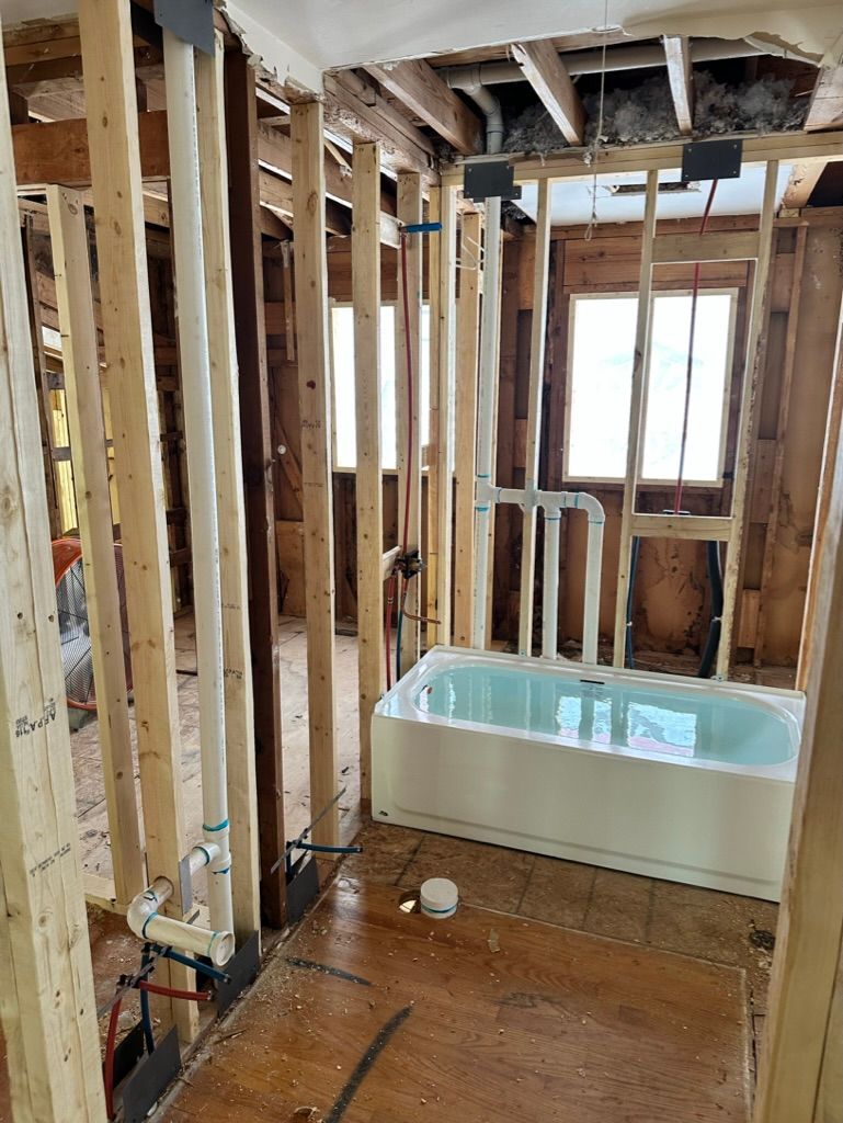 Partially demolished bathroom with exposed studs and a white bathtub under construction