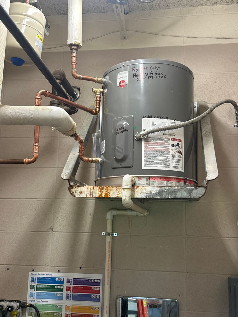 Gray cylindrical water heater with pipes and valves mounted near the ceiling in a utility room