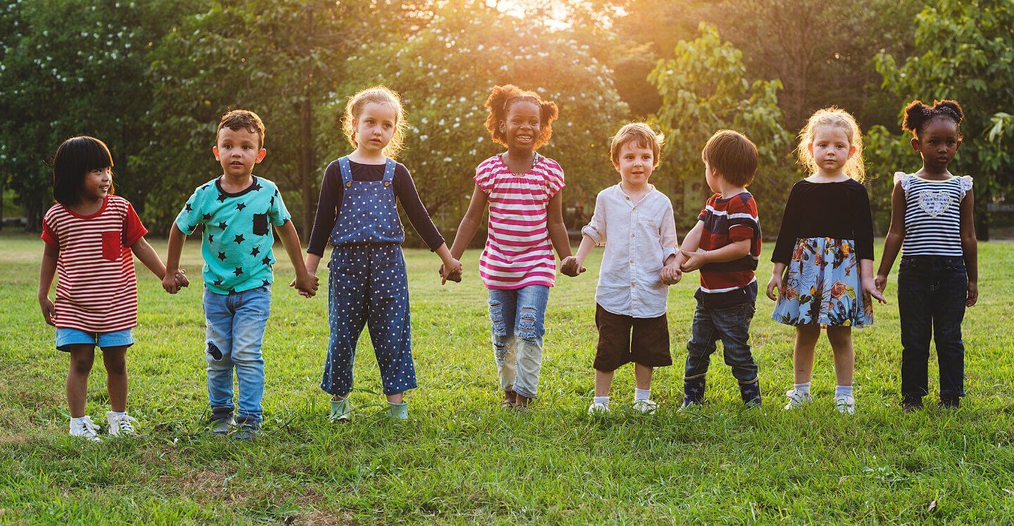 Children holding hands in a grassy field at sunset, standing in a line outdoors.