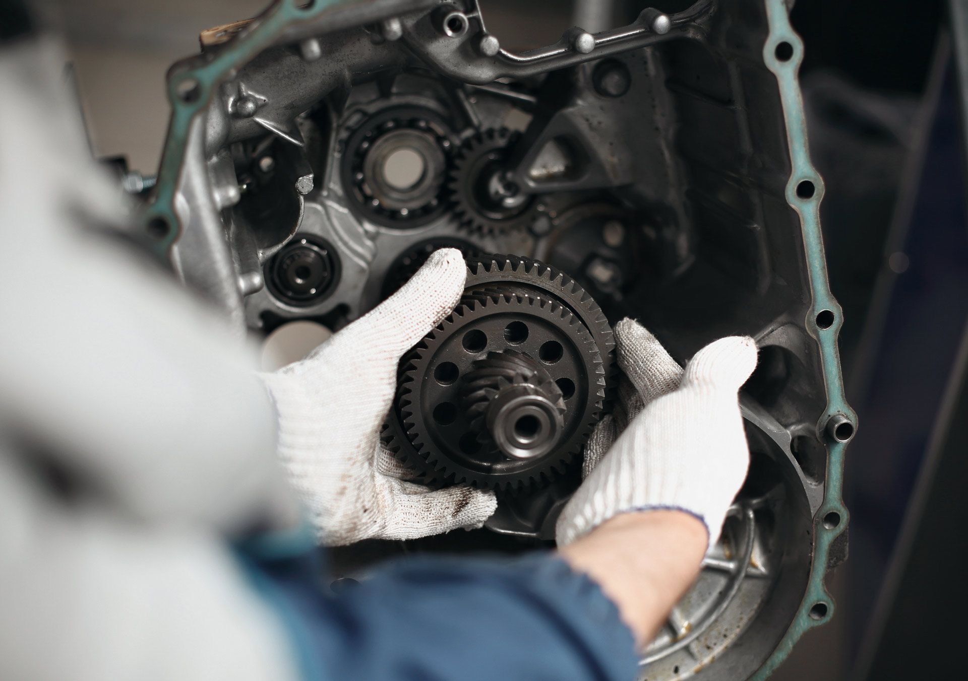 Hands in white gloves assembling gears inside a metal engine casing.