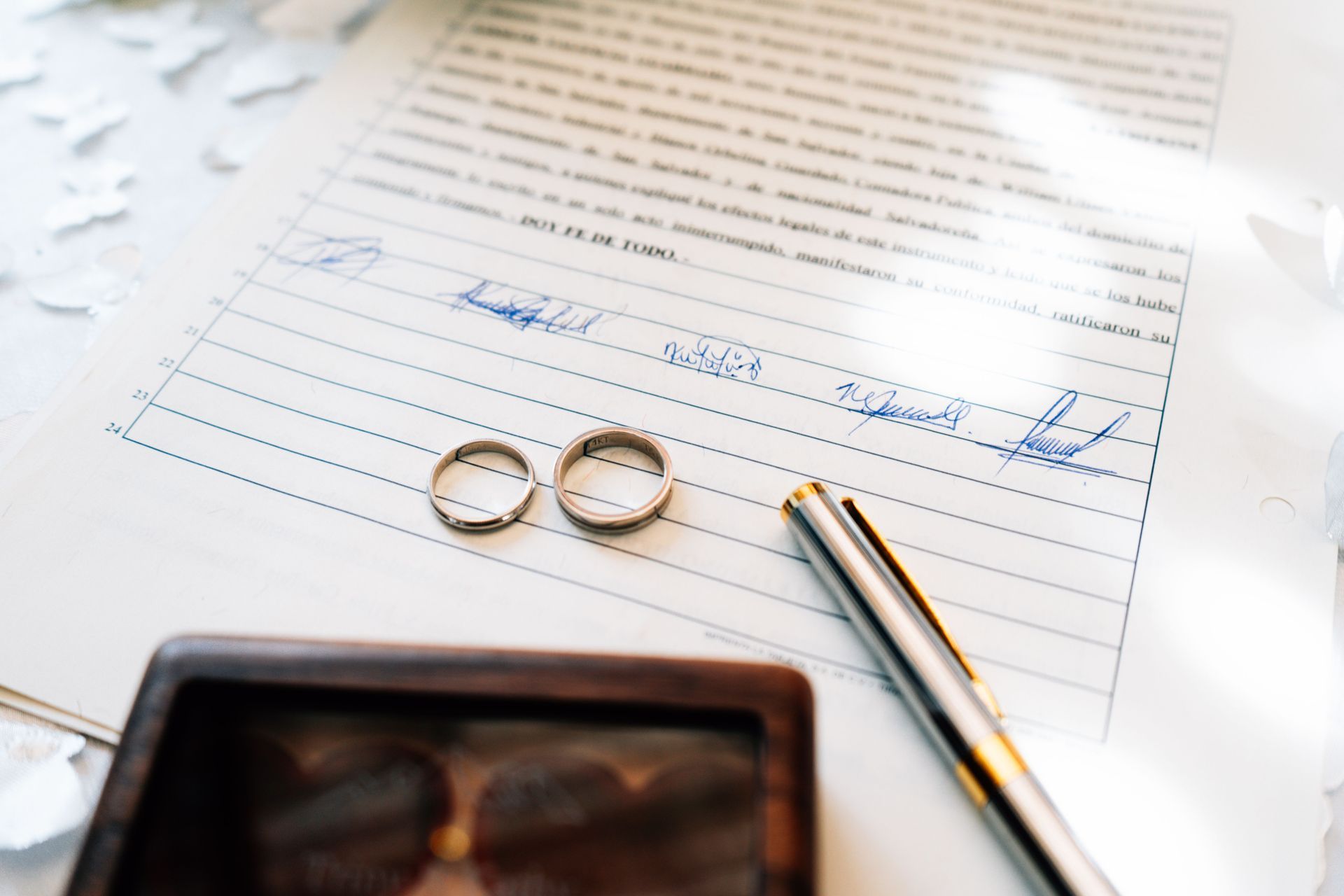 Wedding rings on a lined page with a pen and blurred phone on a desk