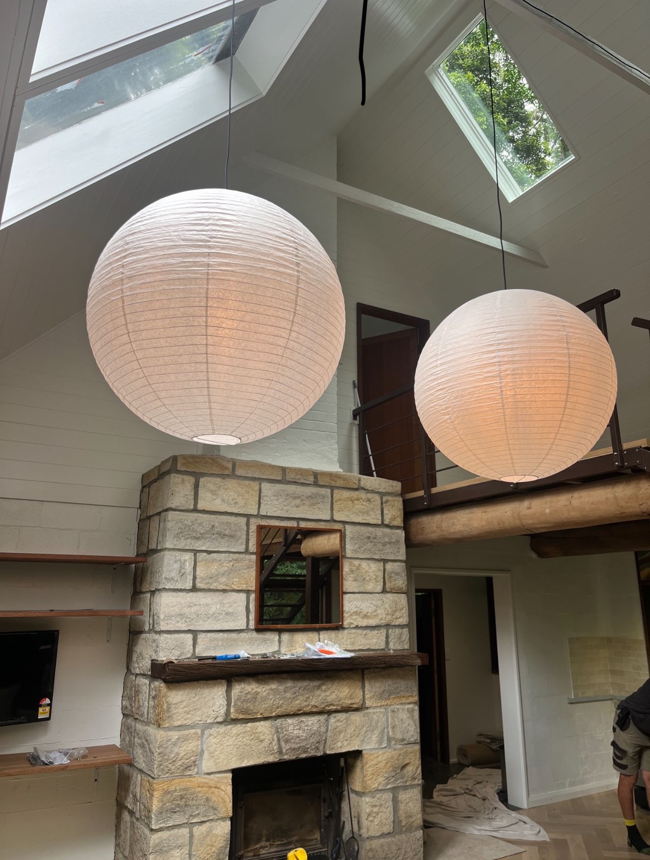 Two round paper lanterns hang over a stone fireplace in a room with a skylight. — DG Electrical & Fire In Kiama, NSW