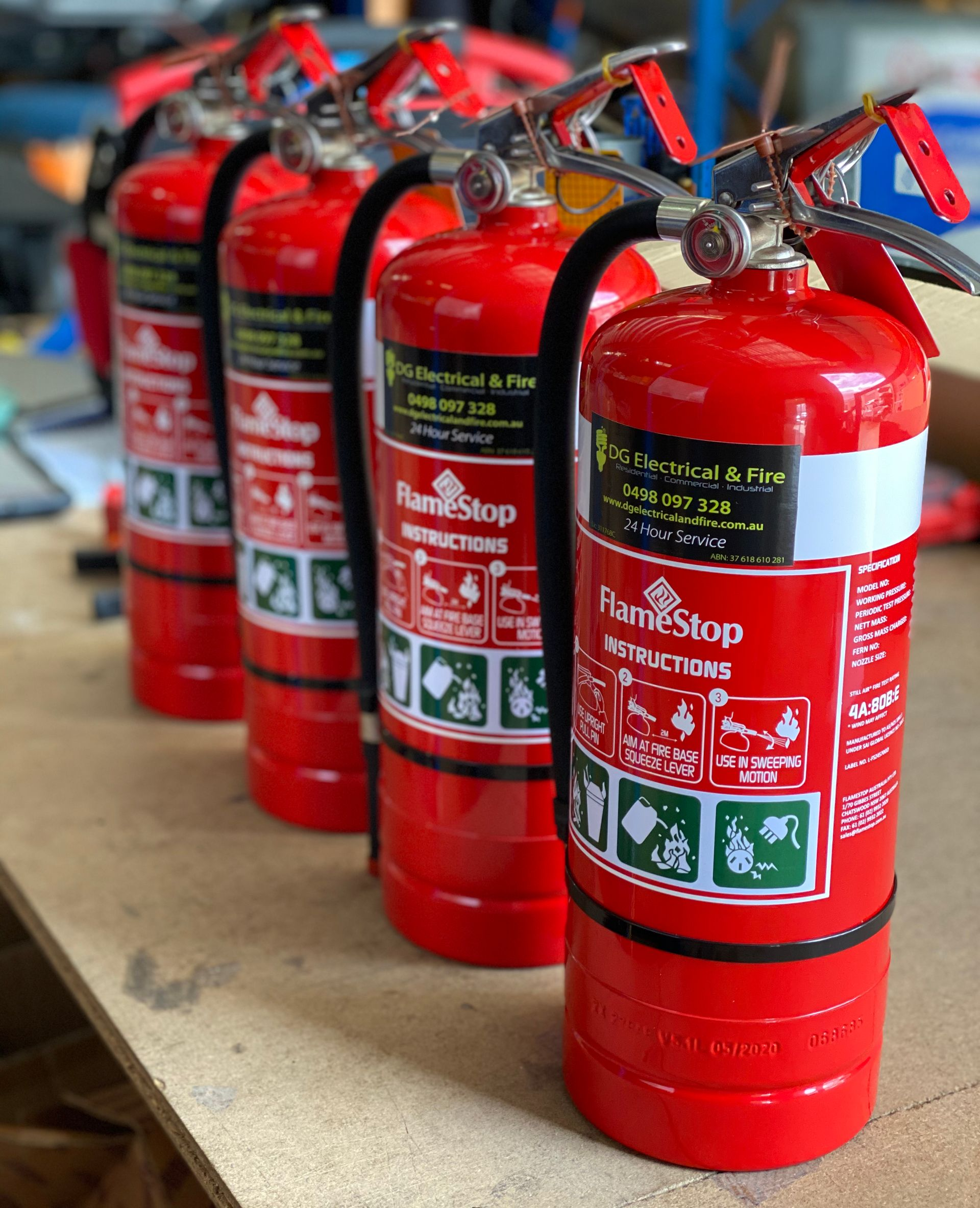 Five red fire extinguishers in a row, labelled with instructions. — DG Electrical & Fire In Kiama, NSW
