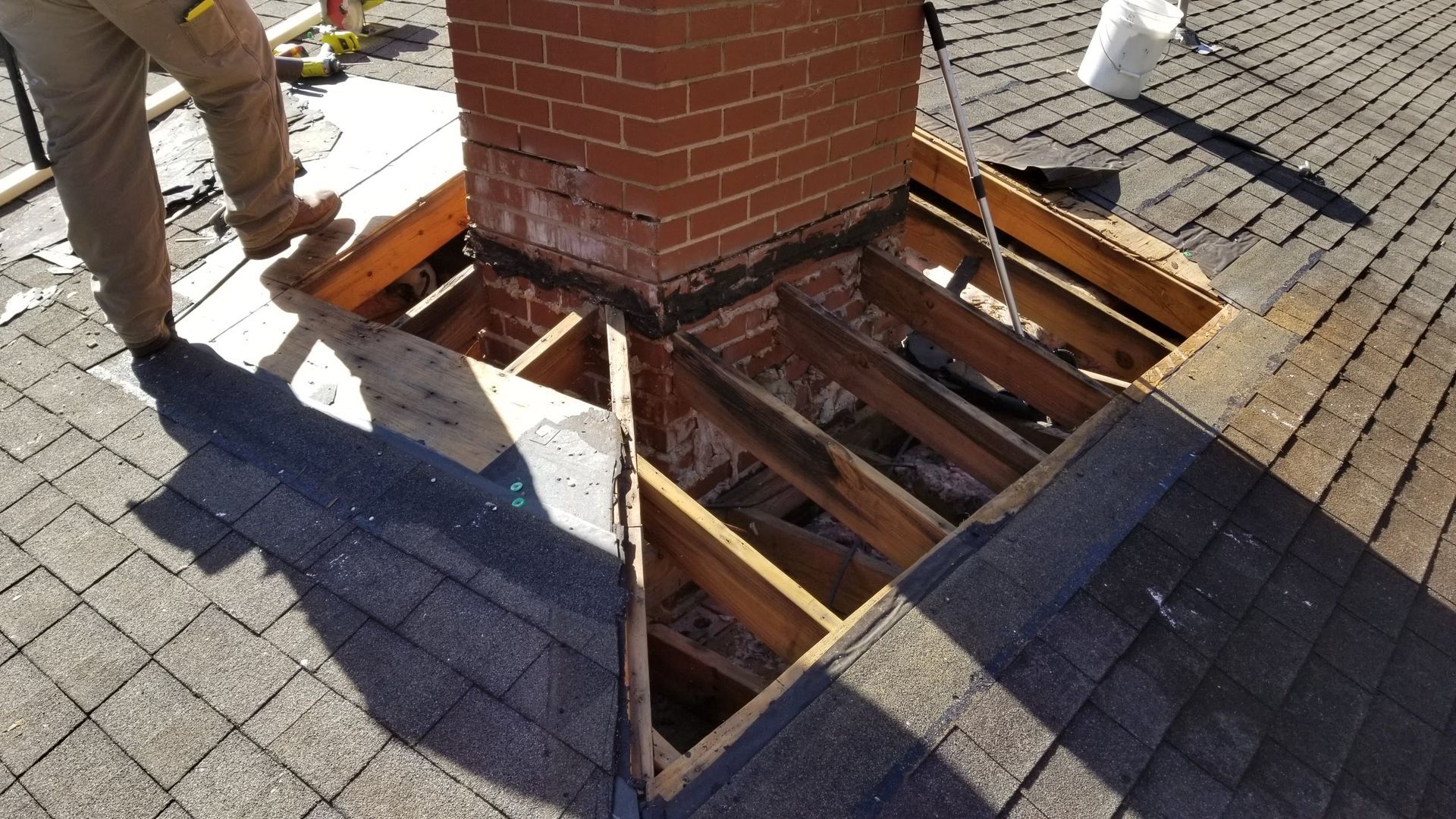 A man is working on a brick chimney on a roof.