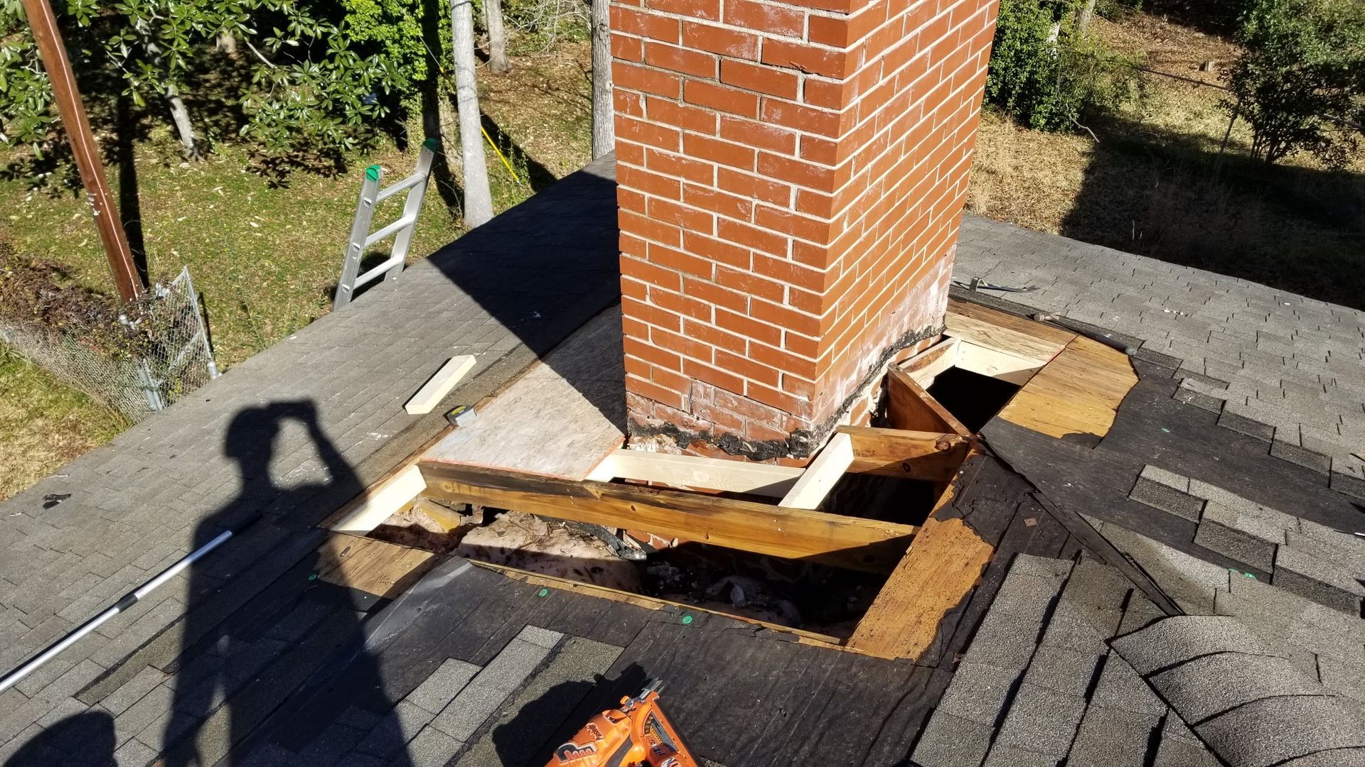 A brick chimney is sitting on top of a roof with a hole in it.