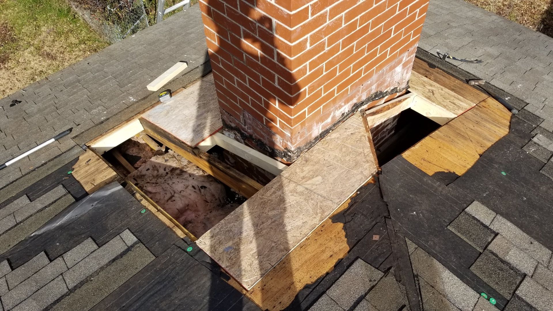 A brick chimney is sitting on top of a roof with a hole in it.