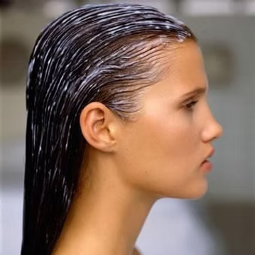 Woman with wet, slicked-back hair; white cream applied. Side profile view.