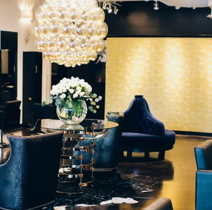 Luxurious salon interior: gold wall, blue velvet furniture, chandelier, floral arrangement, shiny floors.