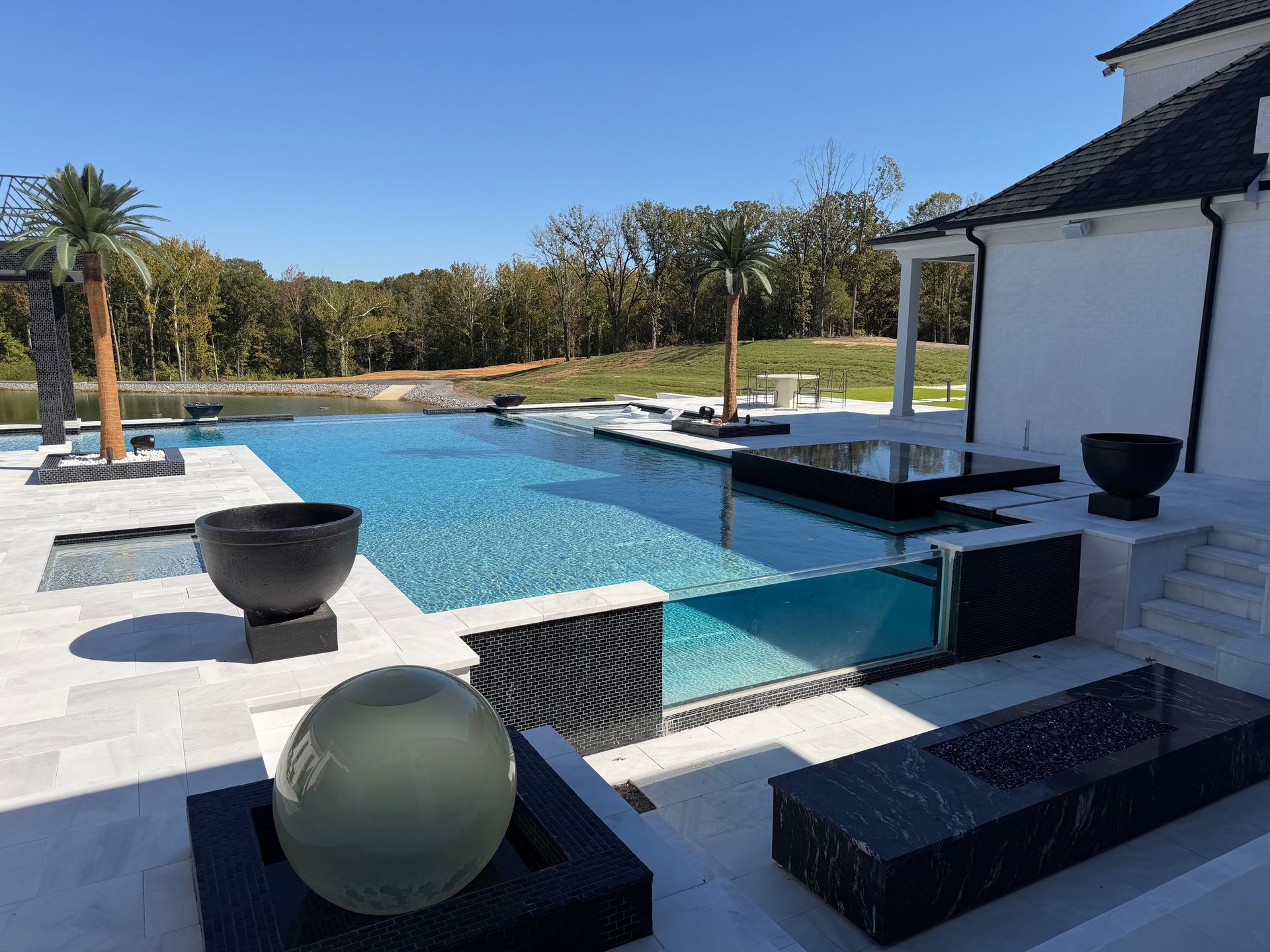 Luxurious backyard pool with clear water, palm trees, and modern architecture under a blue sky.