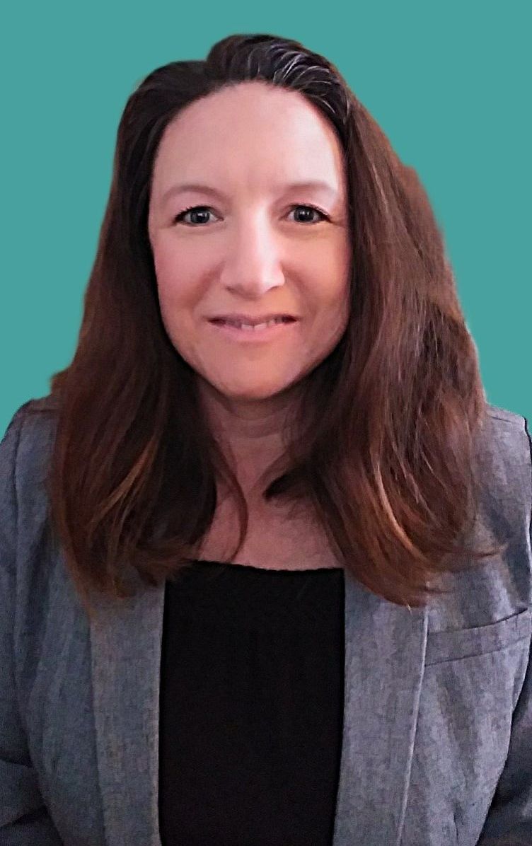 Portrait of a smiling woman with long brown hair, wearing a gray blazer and black top against a teal background