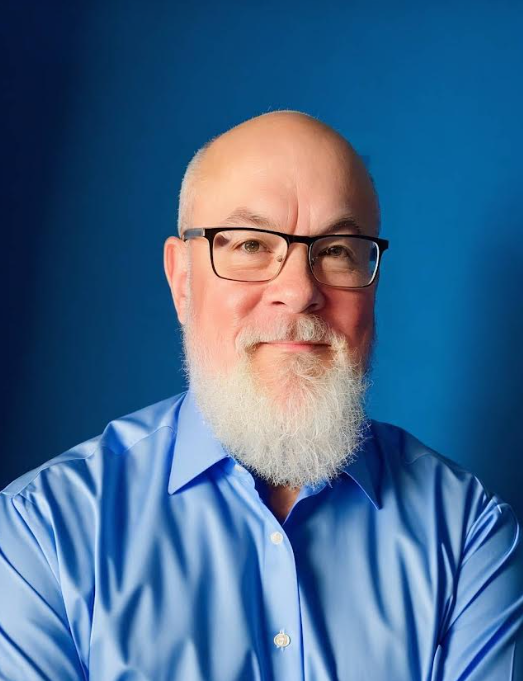 Portrait of a bald man with glasses and a white beard in a blue shirt against a blue background