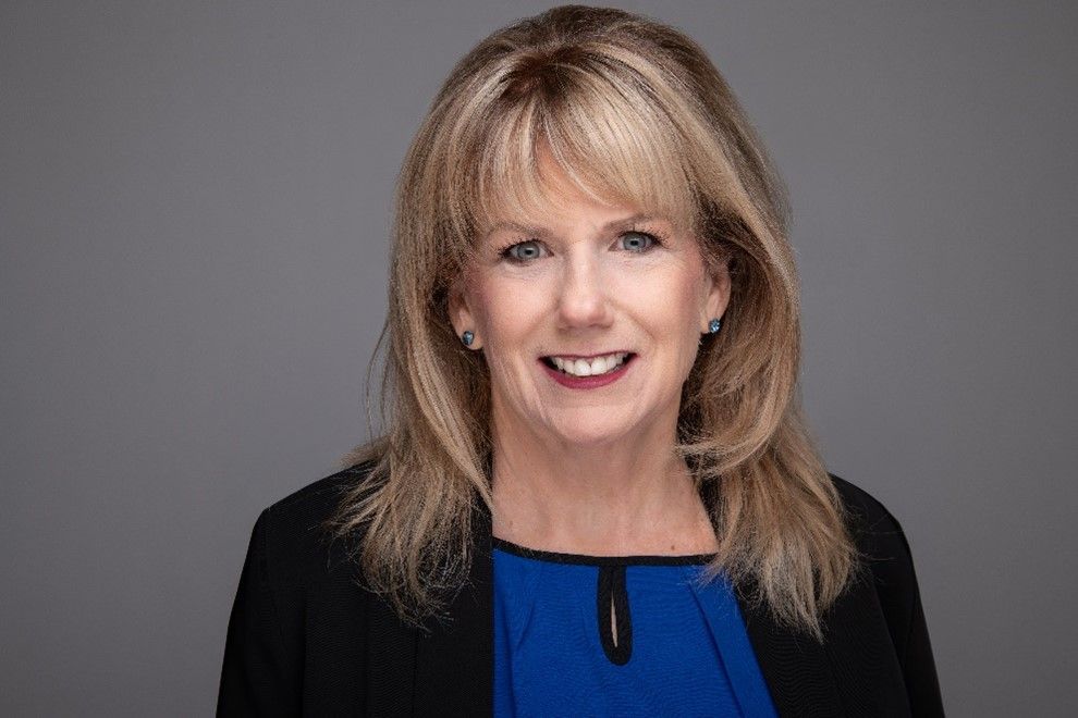 Smiling woman in a black blazer and blue top against a gray background
