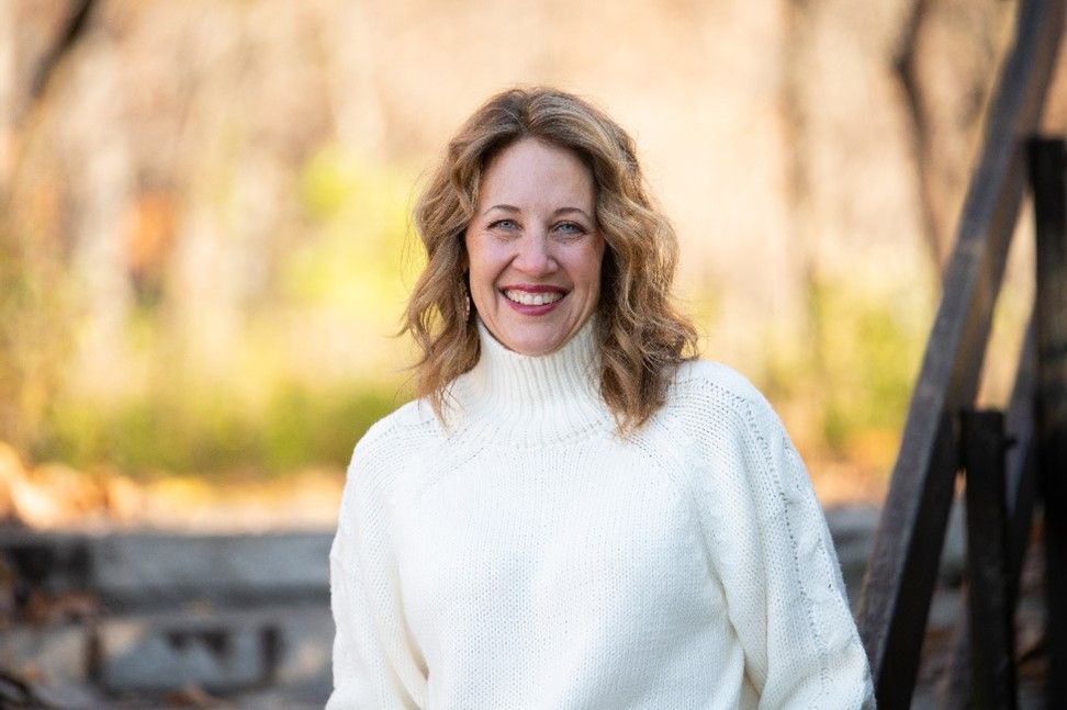 Smiling woman in a white sweater standing outdoors in a blurred autumn setting