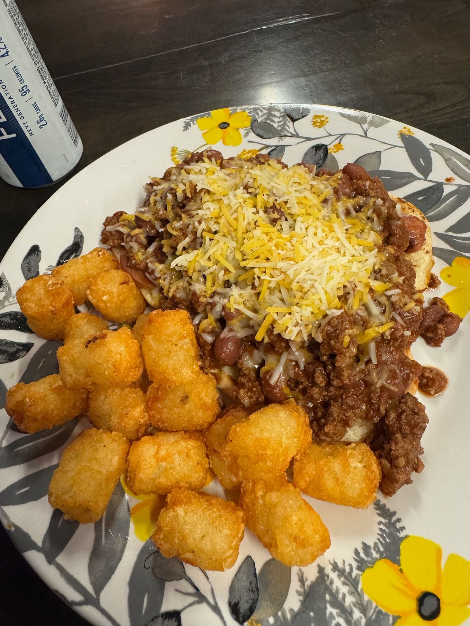 Chili with shredded cheese and tater tots on a floral plate next to a can.
