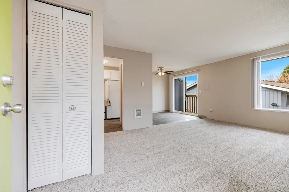 Photo of a living room with plenty of natural light, and the kitchen and dining area in the background